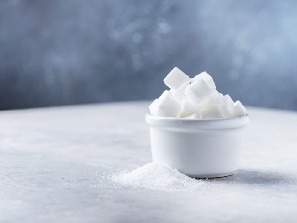 Sugar cubes and grain of sugar on tje light background, selective focus