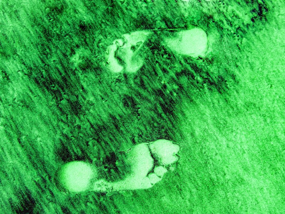 two-footprints-in-the-green-and-black-colored-sand-NPKEWBA