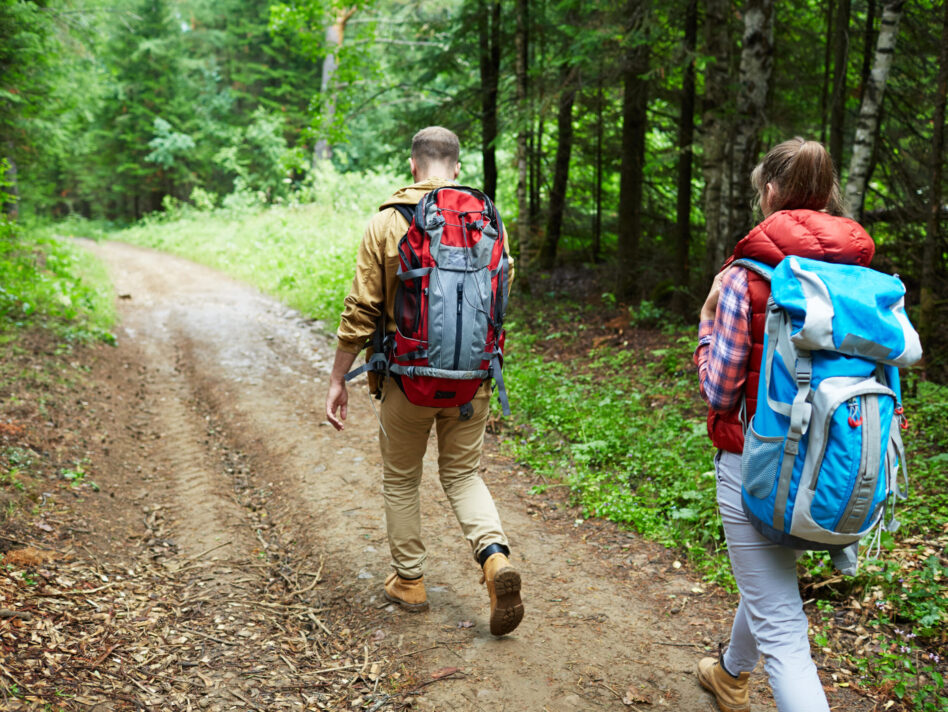 Man and woman with backpacks walking down forest path