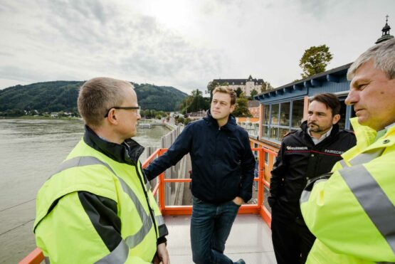 Der behördliche Einsatzleiter Bezirkshauptmann Werner Kreisl, Landesrat Stefan Kaineder, der technische Einsatzleiter Bezirksfeuerwehrkommandant Eduard Paireder und Machlanddamm Geschäftsführer Herbert Froschauer in Grein auf einer Hebebühne zum Aufbau des mobilen Hochwasserschutzes