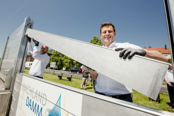 Umwelt- und Klima-Landesrat Stefan Kaineder versucht sich gemeinsam mit Bürgermeister Thomas Punkenhofer im Aufbau des mobilen Hochwasserschutzes in Mauthausen.