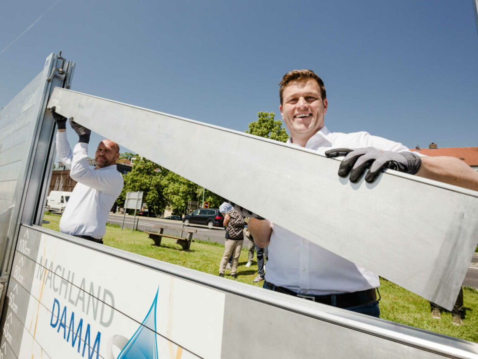 Umwelt- und Klima-Landesrat Stefan Kaineder versucht sich gemeinsam mit Bürgermeister Thomas Punkenhofer im Aufbau des mobilen Hochwasserschutzes in Mauthausen.