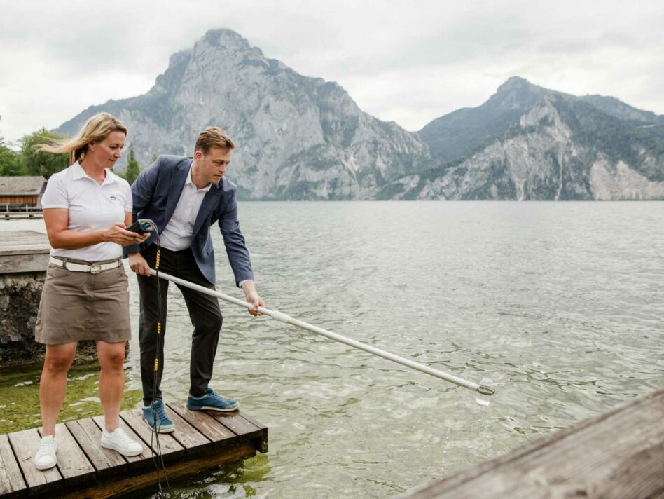 Ing.in Sabine Kapfer von der Gewässergüteaufsicht des Landes OÖ zeigt Umwelt- und Klima-Landesrat Stefan Kaineder die Probenahme zur Überprüfung der Badequalität am Traunsee.